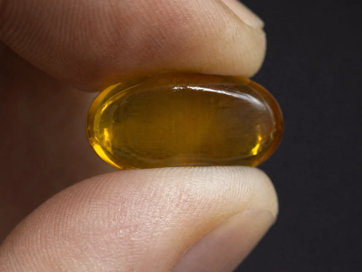 Macro photograph of a rigid glassy amber hard candy squeezed between a thumb and forefinger, keeping its shape completely with no dimple and no embossing.